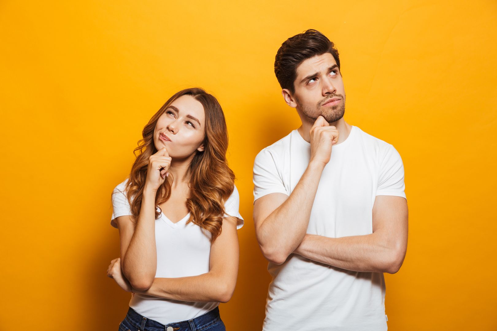 Image of happy young people man and woman in basic clothing thinking and touching chin while looking aside isolated over yellow background