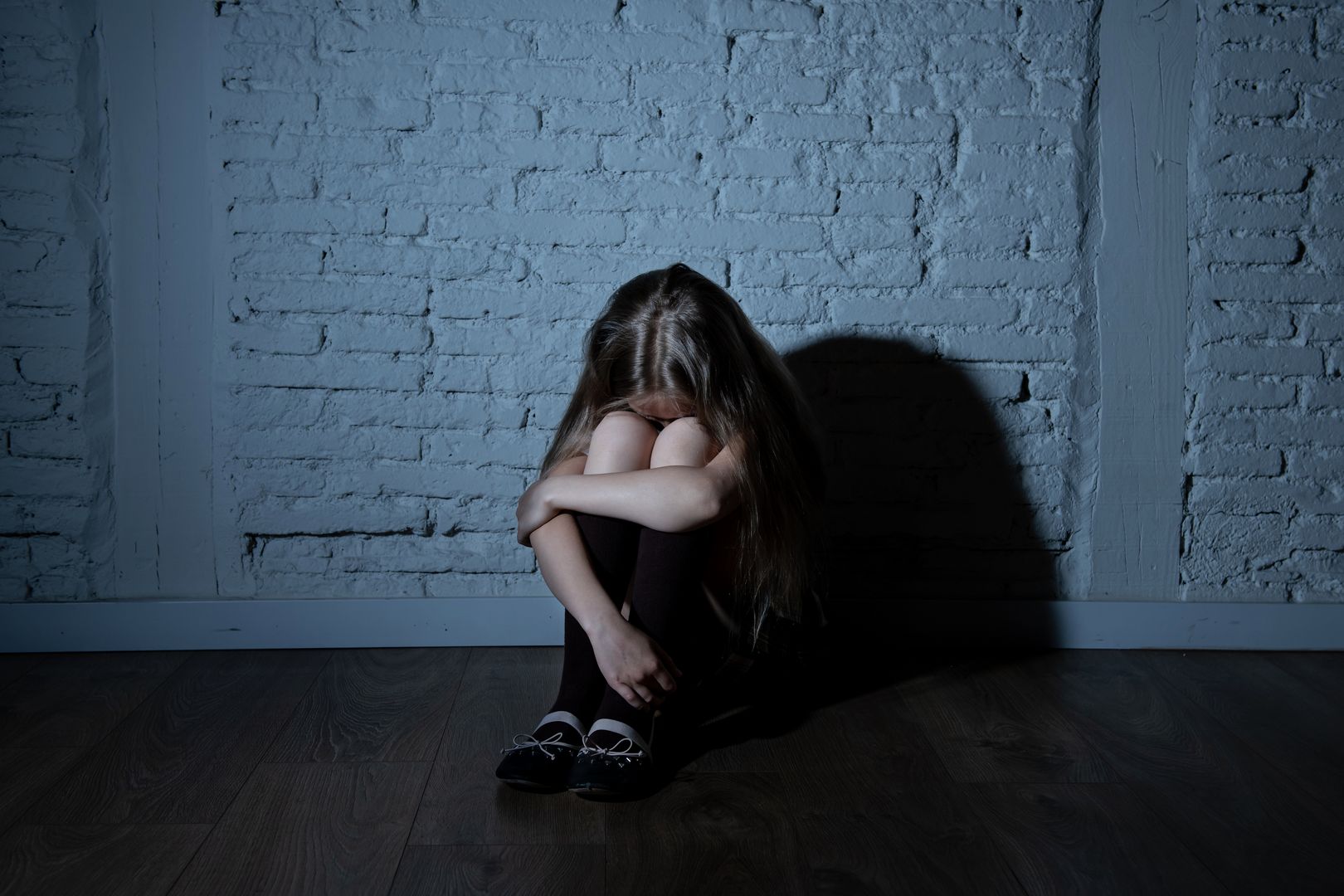 Sad desperate young girl suffering from bulling and harassment felling lonely, unhappy desperate and hopeless sitting against the wall, dark light. School isolation, abuse and bullying concept (Sad desperate young girl suffering from bulling and haras