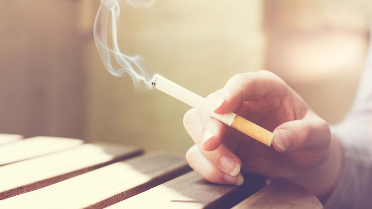 Woman smoker smoking a filter tip cigarette with her hand resting on a slatted wooden table with copy space, close up view