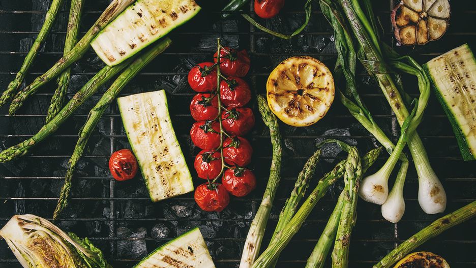 Grilled vegetables green asparagus, garlic, lemon, spring onion, zucchini, cherry tomatoes, salad on bbq grill rack over charcoal. Top view. Barbecue concept