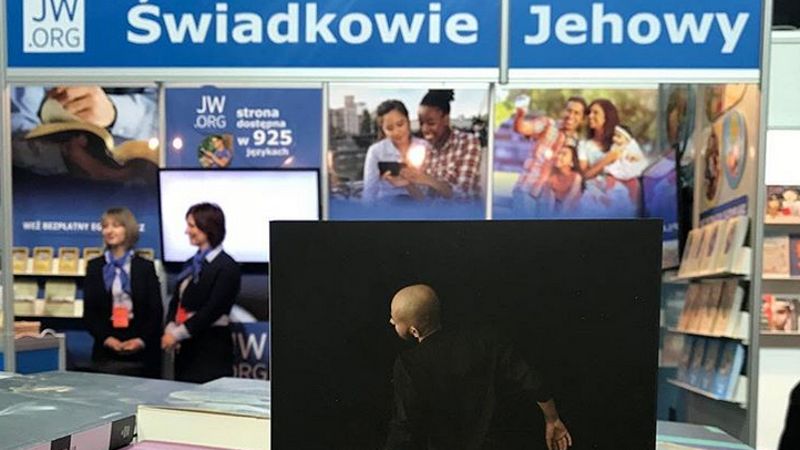 Mocne zdjęcie autorstwa Mariusza Szczygła. Stoisko Świadków Jehowy zestawione z książką o tej wspólnocie
