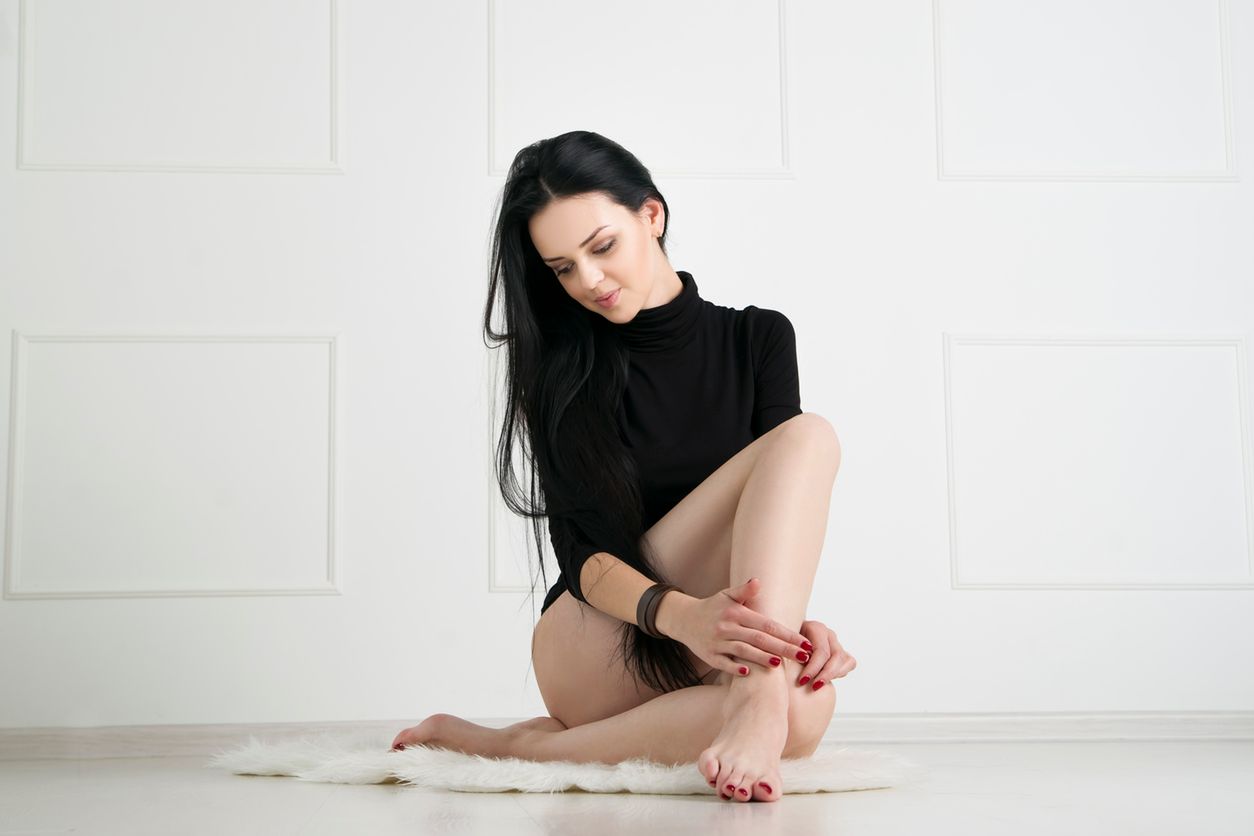 Beautiful young woman with long legs in bodysuit sits on the floor 