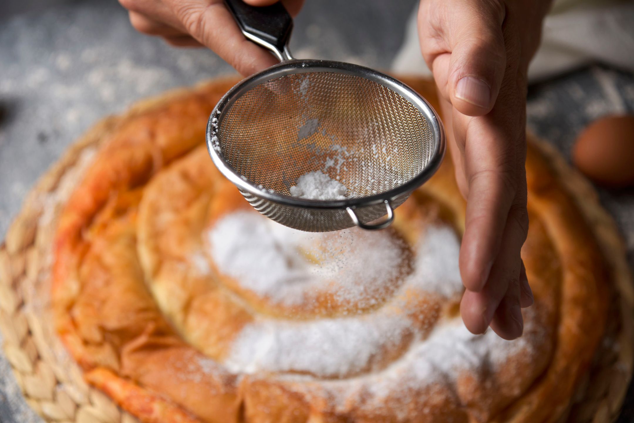 closeup of a young caucasian man sprinkling powdered sugar on an ensaimada, a pastry typical of Mallorca, Spain, placed on a rustic wooden table 
