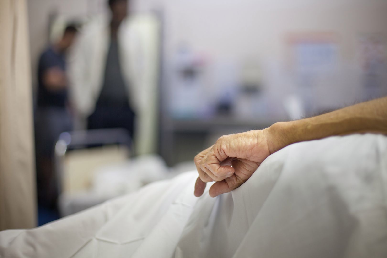 An old man's hand rests at his side in a hospital bed
