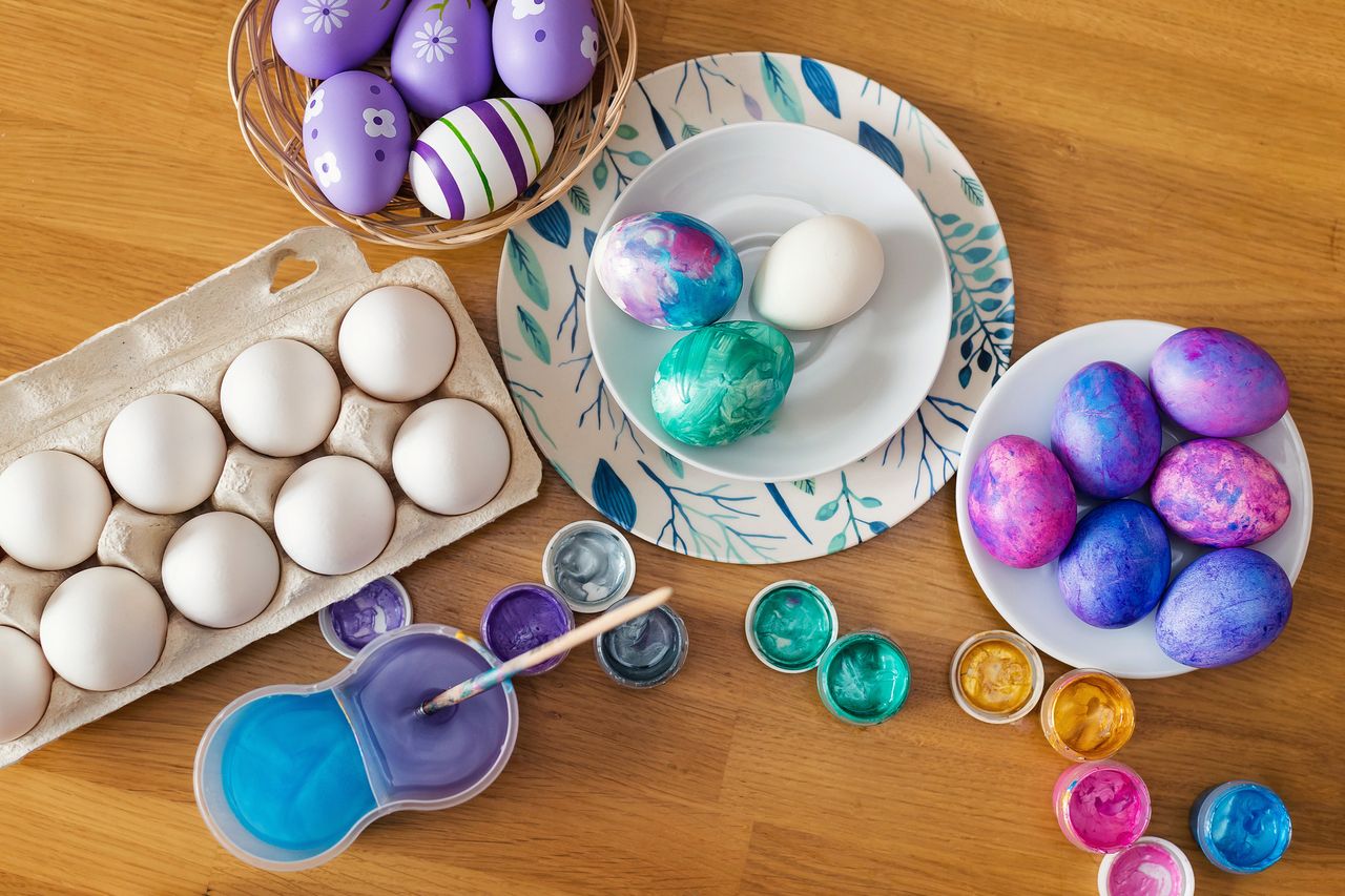 On the wooden table there are plates with eggs for decoration and colorful paints with a brush. Coloring Easter eggs, preparing for the celebration of Easter.