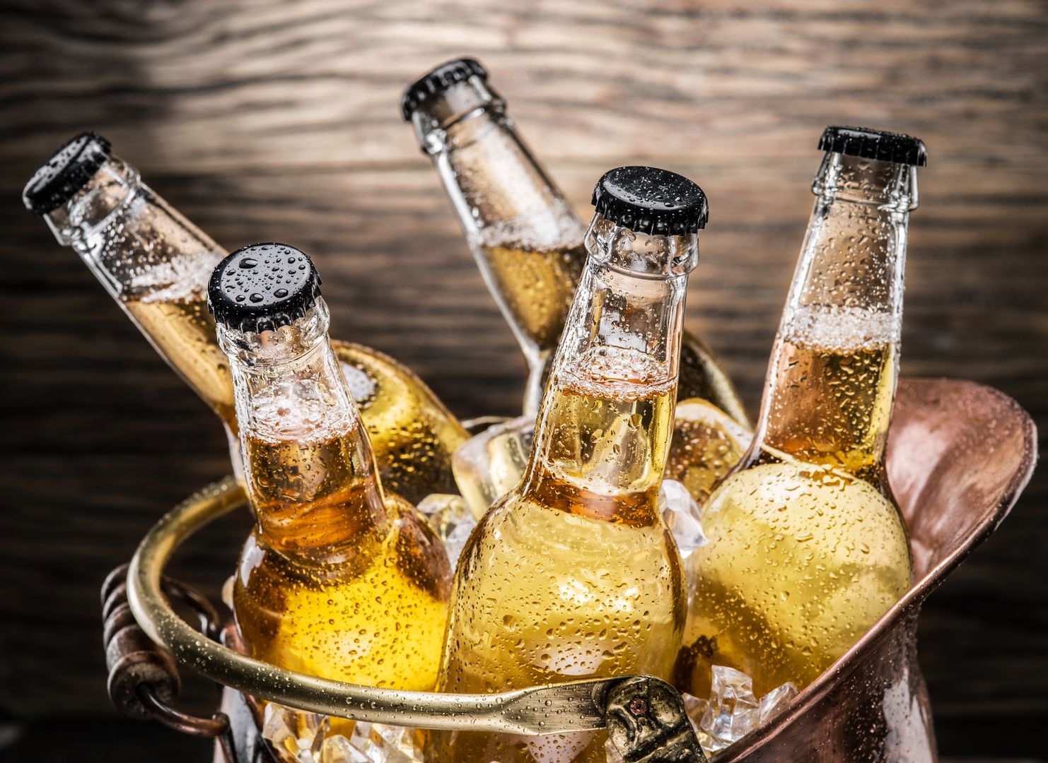 Cold bottles of beer in the brazen bucket on the wooden table.