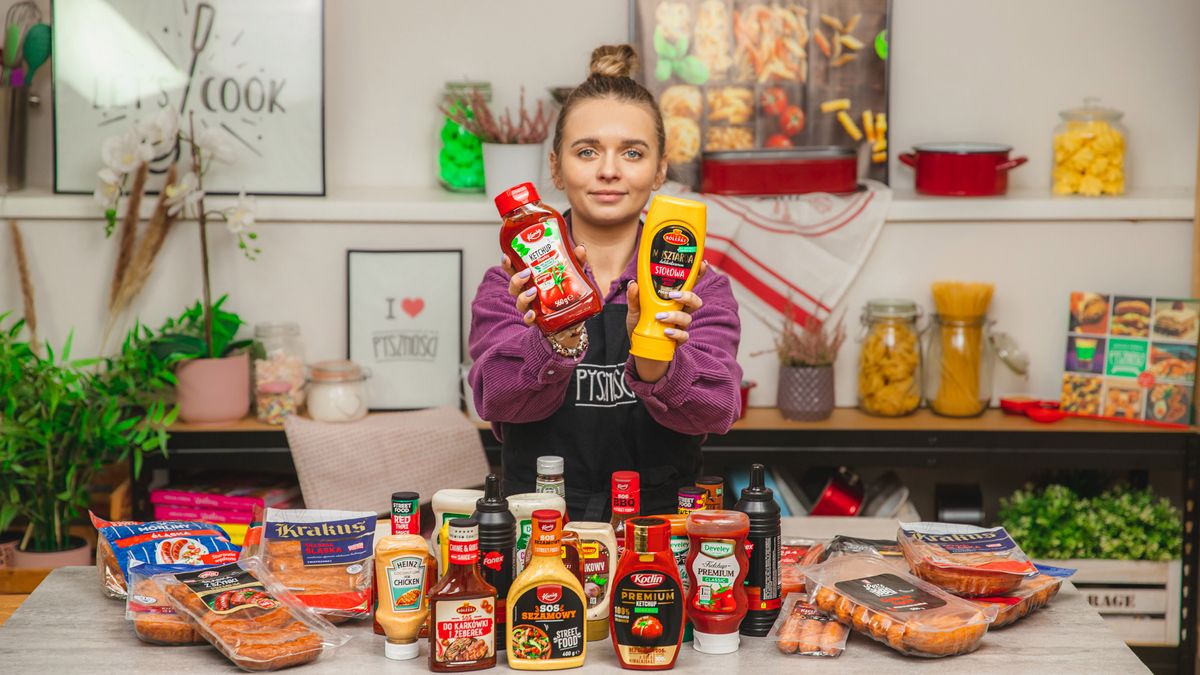 Kobieta trzyma dwa sosy w dłoniach. Na blacie przed nią stoją butelki z różnymi sosami