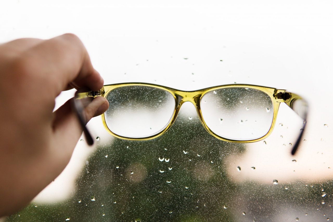 Reading glasses in hand on window background