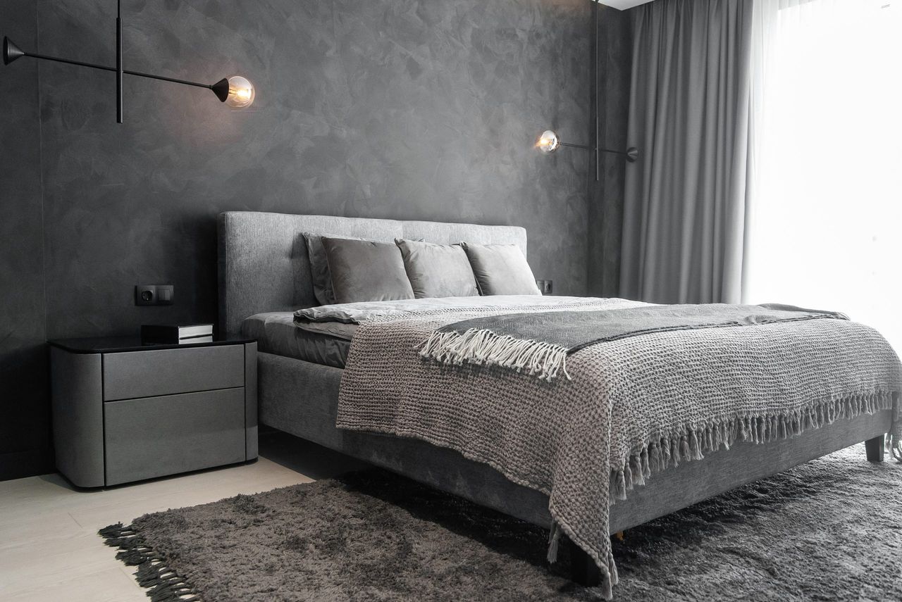 Master bedroom for a lonely stylish man, a bachelor. Modern room with trendy gray interiors, large king-size and stylish lamps.