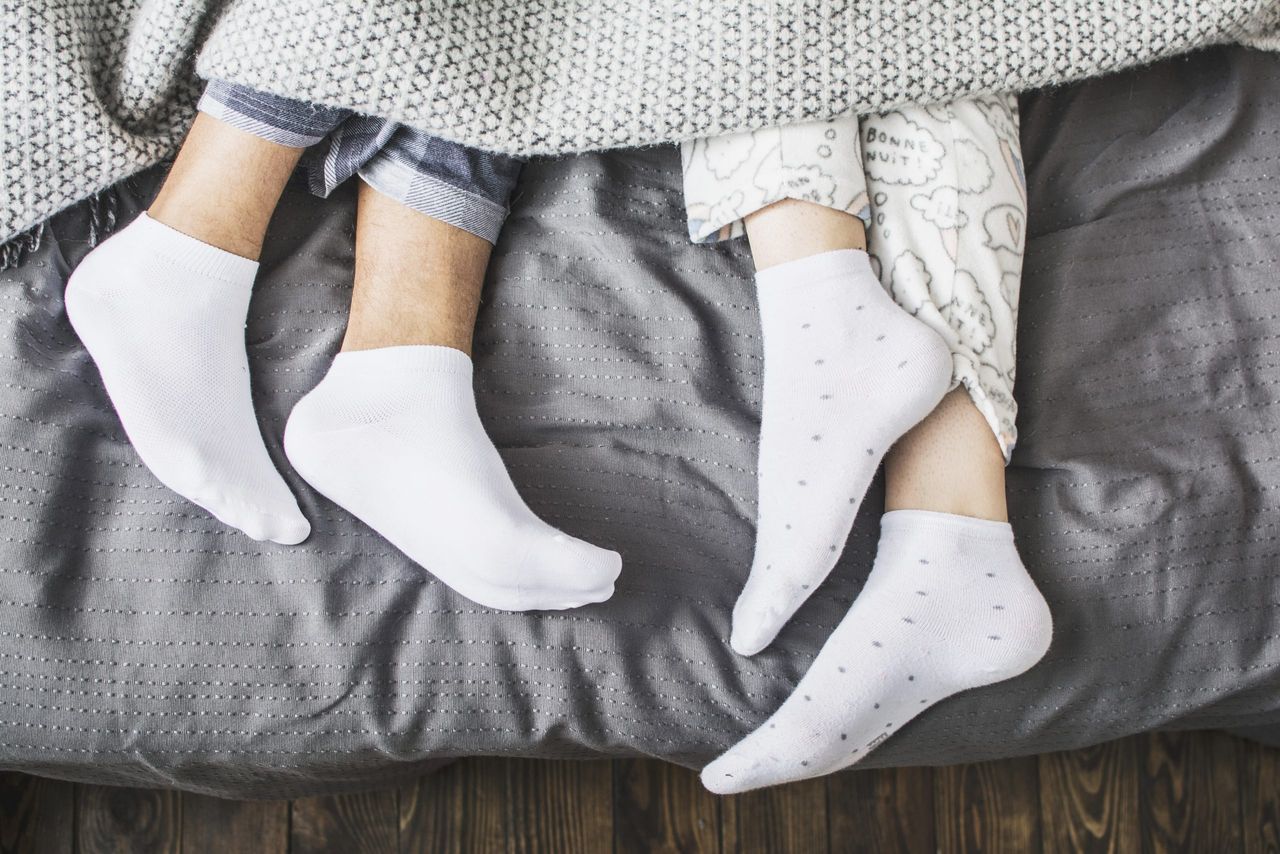 male and female legs in socks under a blanket in a bed