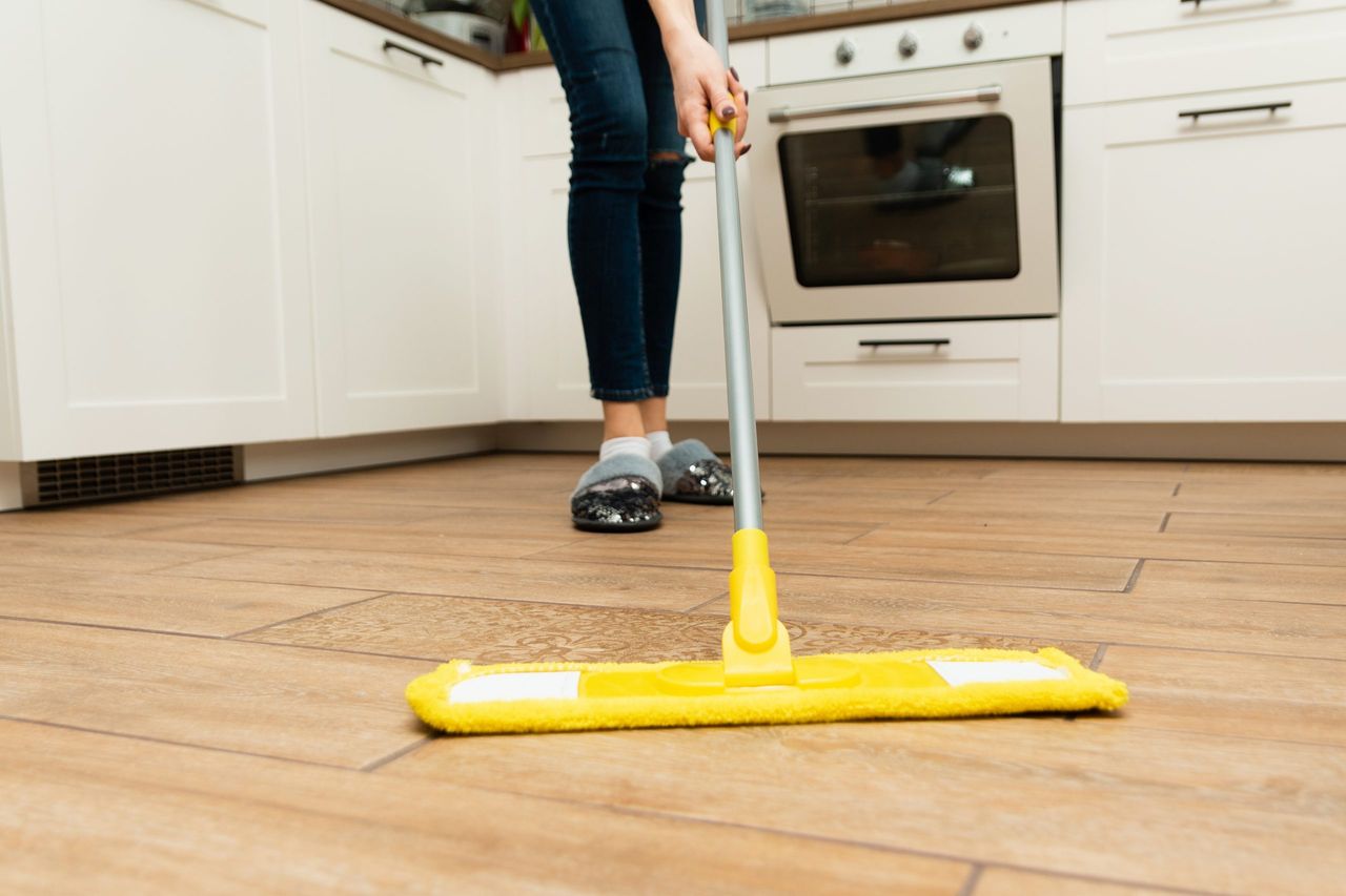 Worth housewife cleaning floor at home. Lovely woman washes wooden floors from a laminate in a bright kitchen.