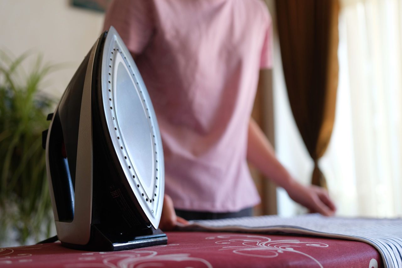 Close-up of woman housewife ironing striped bedsheet on board using steam iron. Female doing housework. Housekeeping and household chores concept