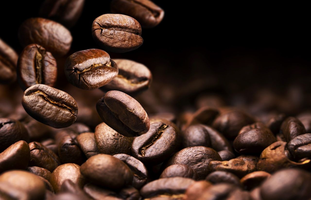 Roasted coffee beans falling on pile, black background with copy space, close up