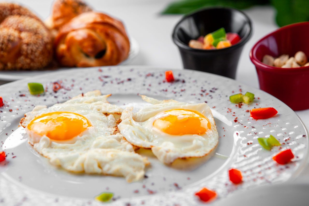 Fried eggs in a plate with a pastry on background. top view.