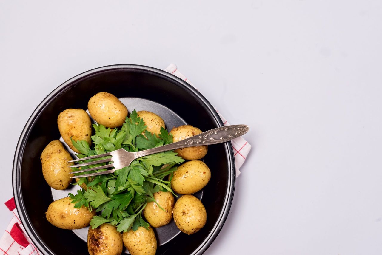 Black Plate of Organic Young Roasted Potatoes Decorated with Parsley Blue Background Top View