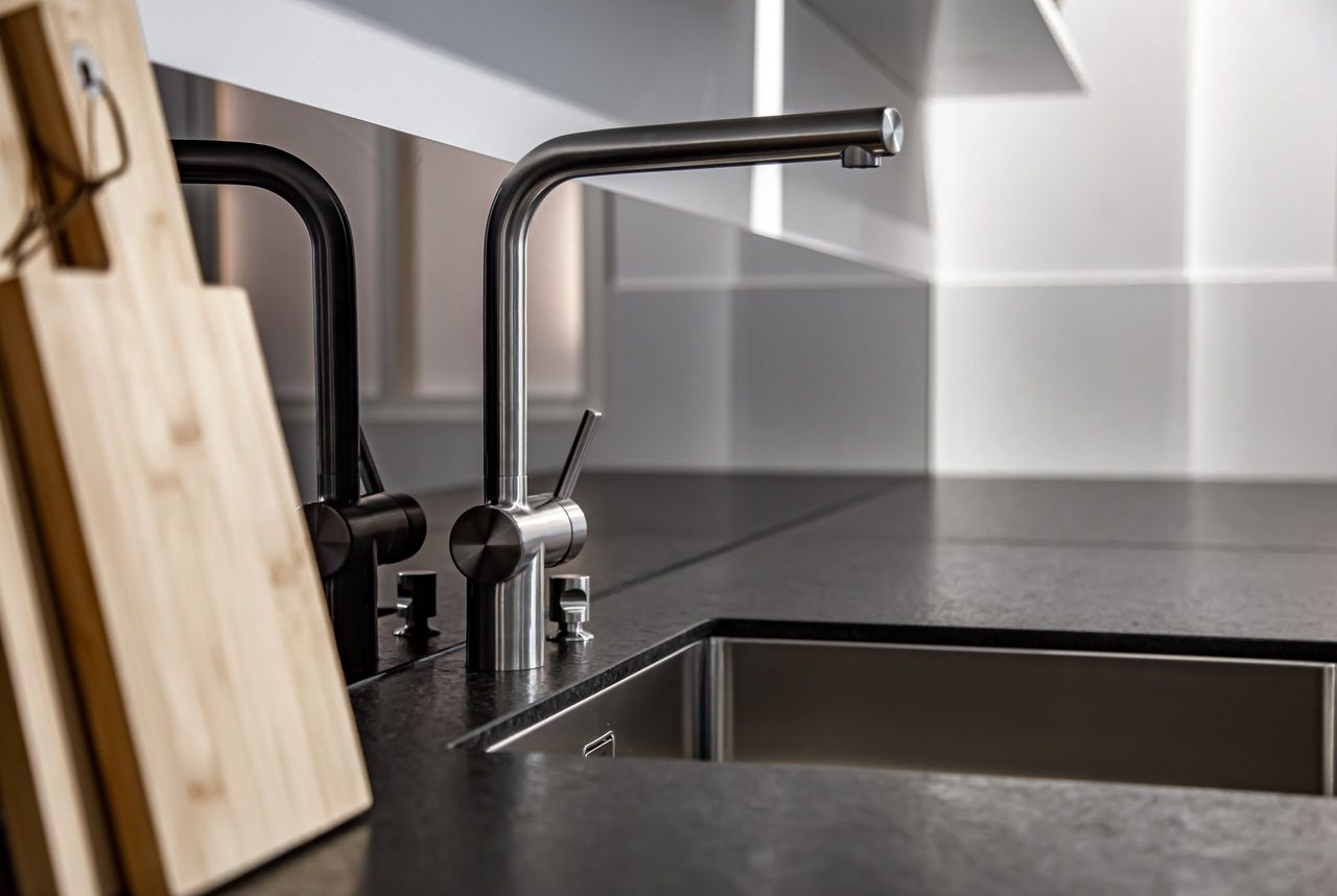 Modern designer chrome water tap over stainless steel kitchen sink close up.