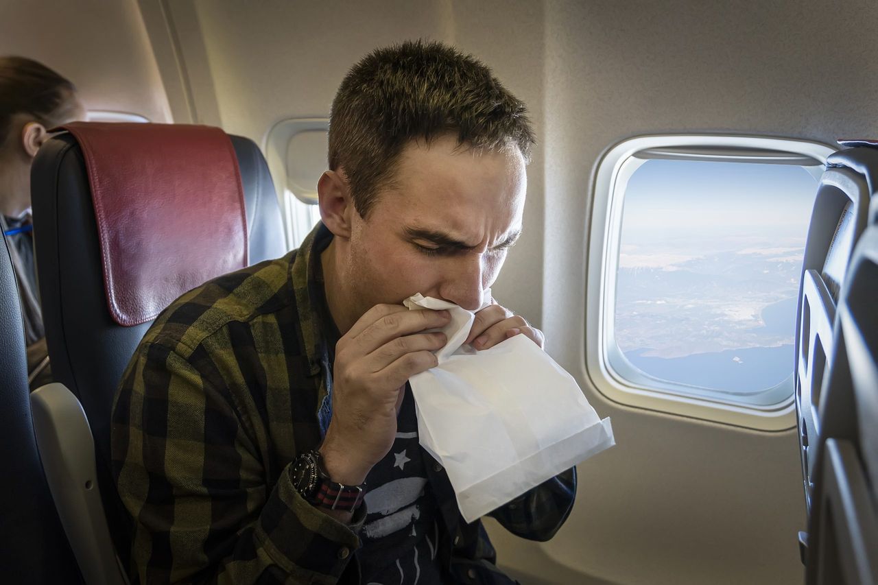 Nervous young man with aviophobia breathing into paper bag in airplane. Nausea during the flight. A young guy gets carsick in transport.