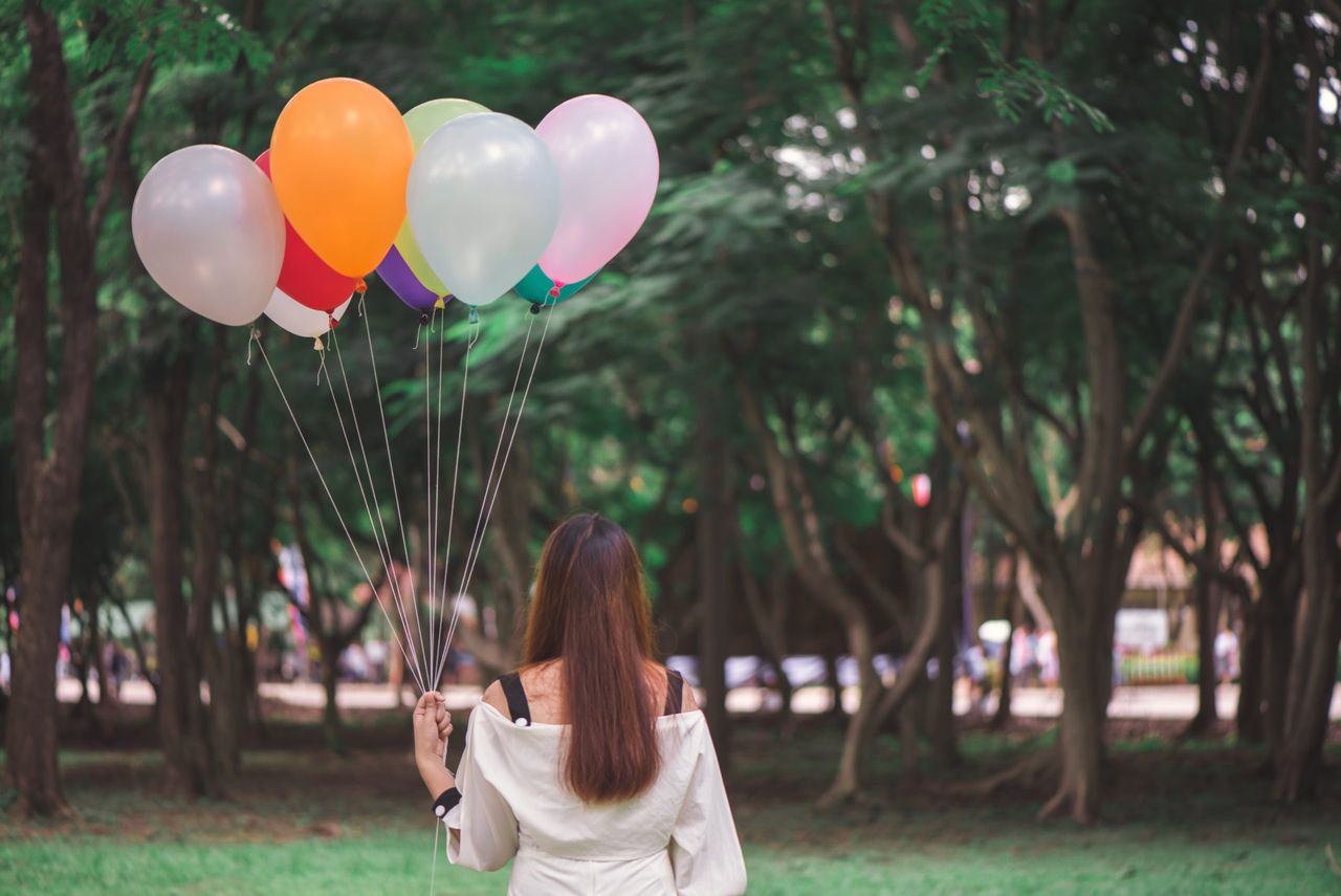 Smiling young beautiful asian women with long brown hair in the park. With rainbow-colored air balloons in her hands.sunny and positive energy of nature.