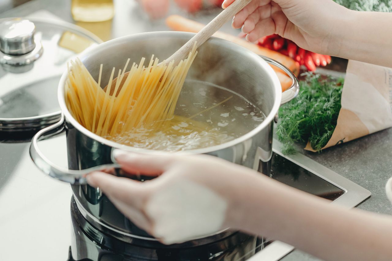 Girl cooking pasta in the kitchen, bowling pasta in pot.