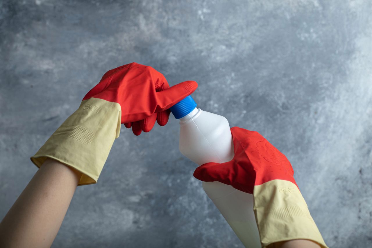 Hands in red gloves opening container of bleach. High quality photo