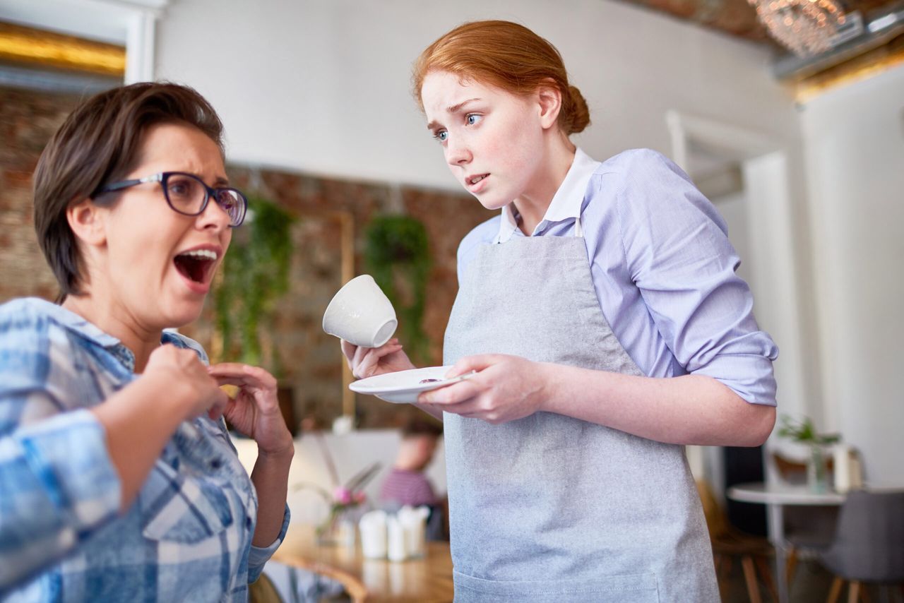 Clumsy waitress spilled hot tea from cup on her client