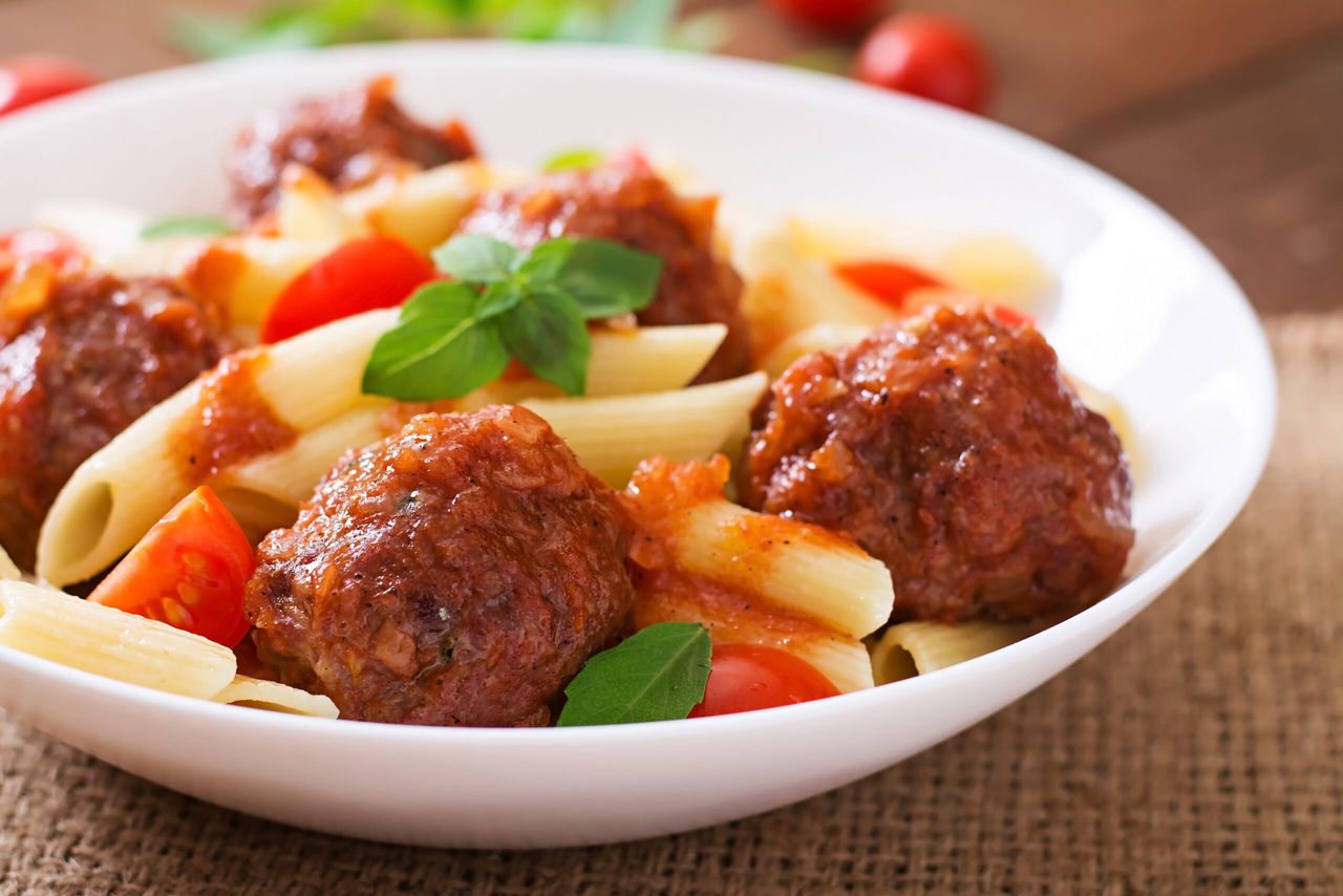 Penne pasta with meatballs in tomato sauce in a white bowl