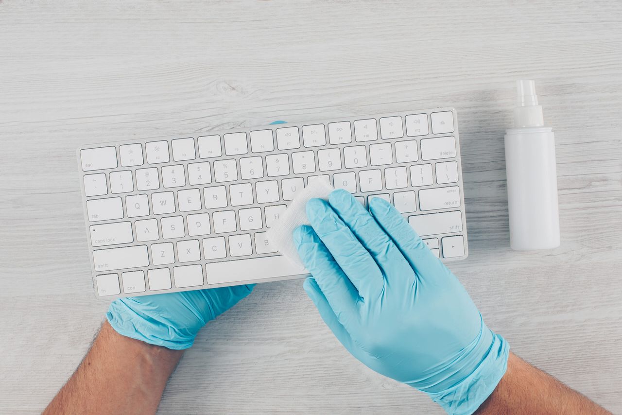 A man in gloves sanitizing a keyboard in light wooden background with sanitizer. coronavirus