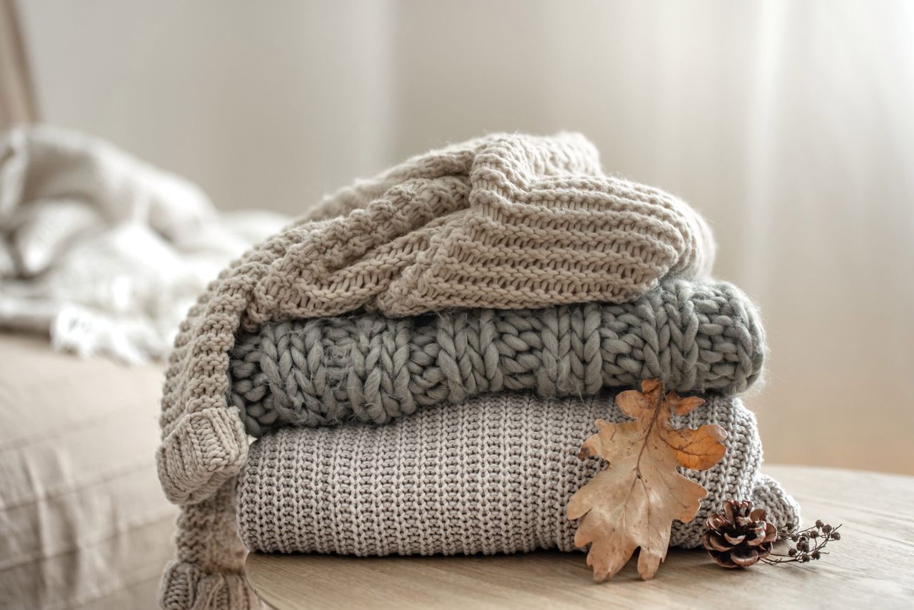 Autumn composition with cozy knitted sweaters in pastel shades and a dry leaf.