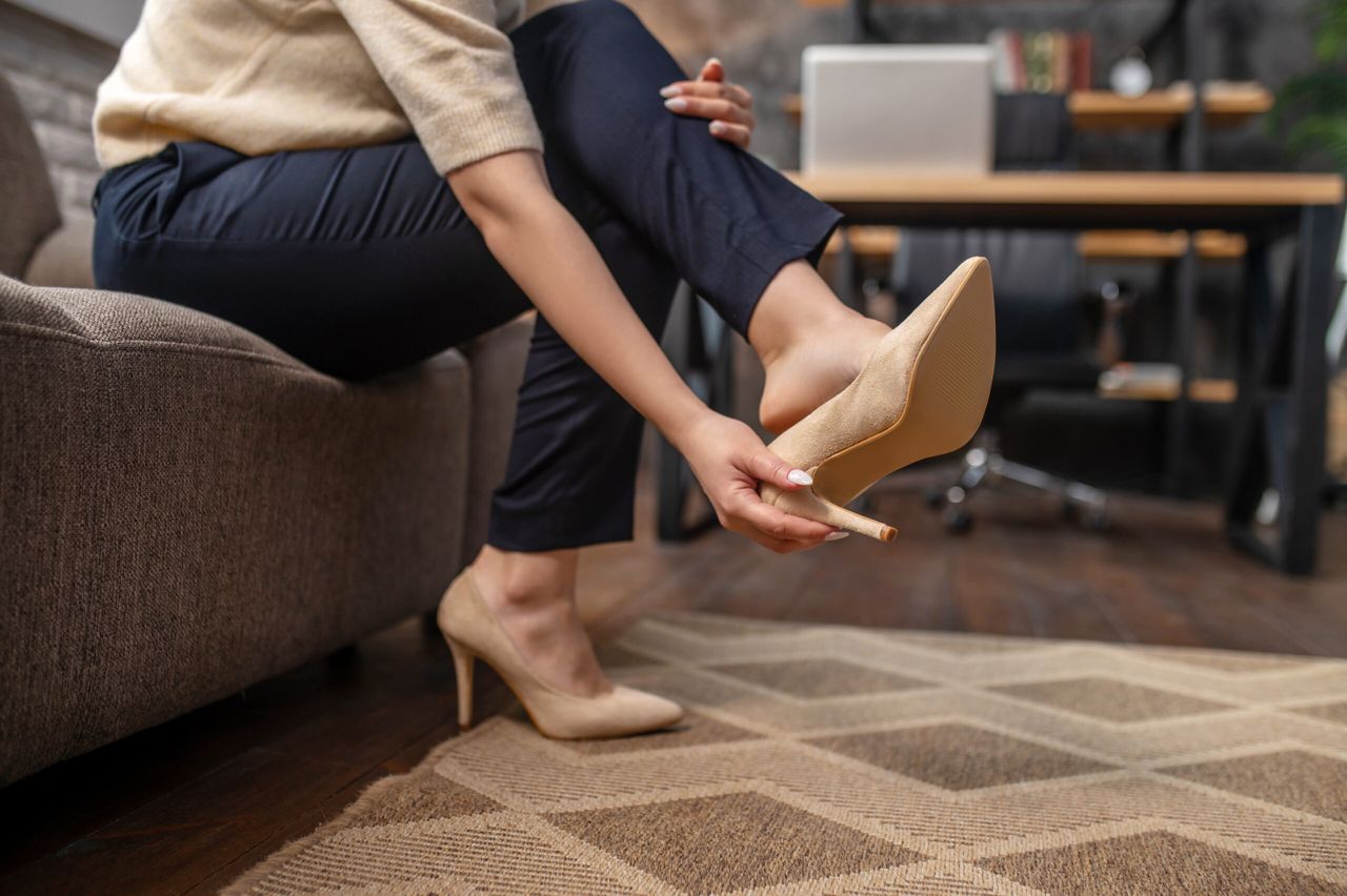 Cropped photo of a woman sitting on the sofa and taking off her high-heels on the carpet