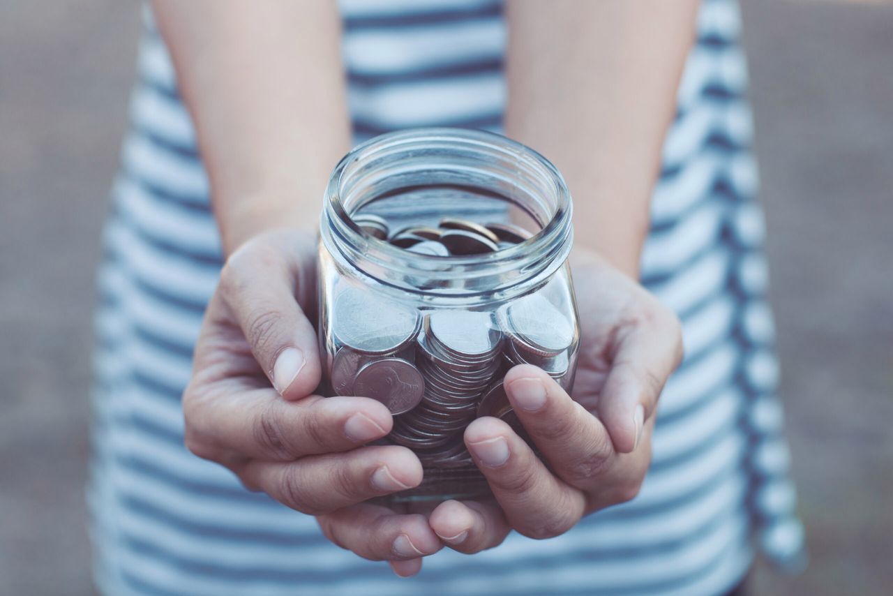Young woman holding coin in glass bottle in hands as saving money and charity concept