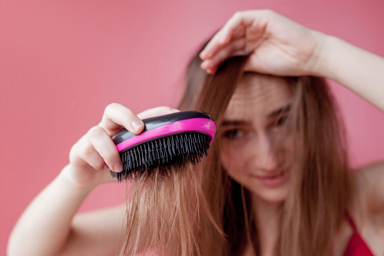 Young beautiful girl having problems while hair on pink background.