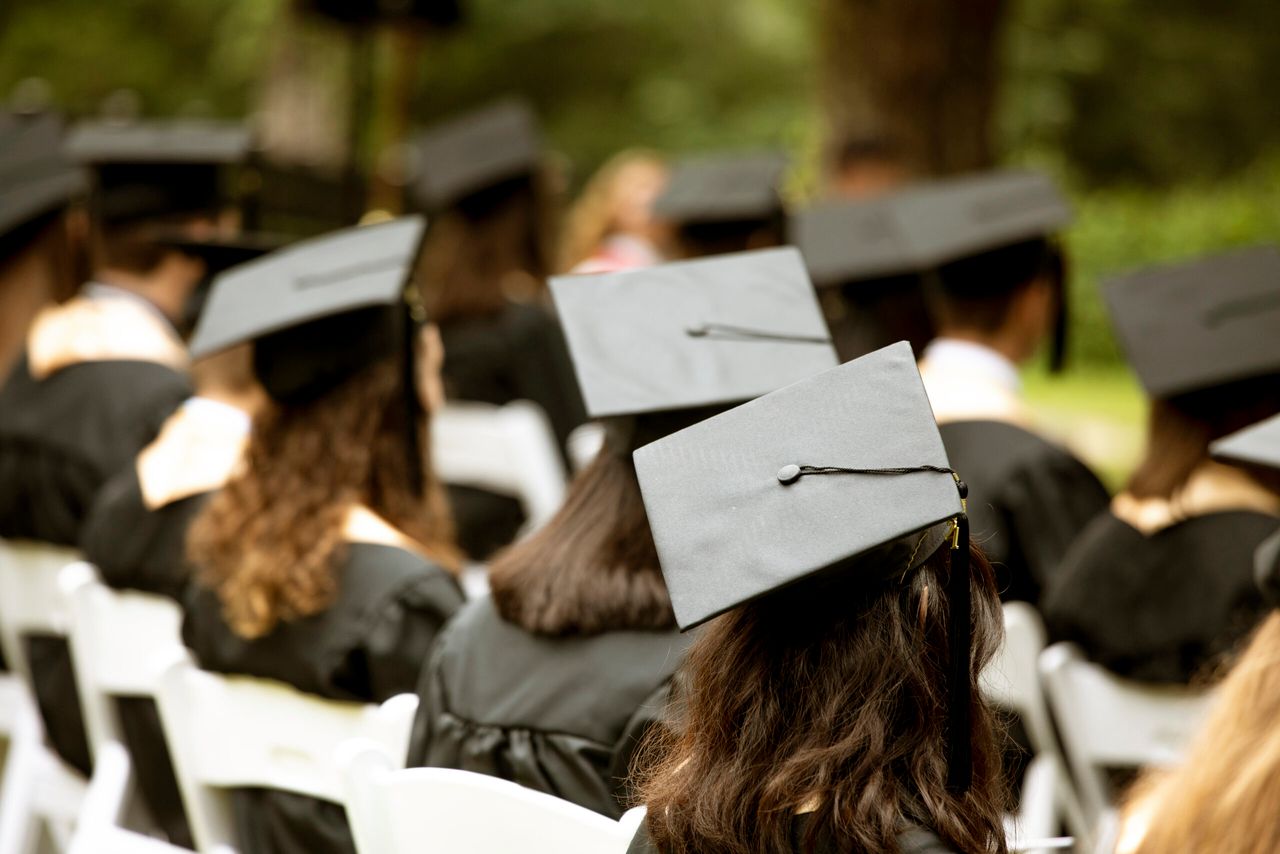 A group of students sit at a graduation ceremony, focus on mortarboard hat.