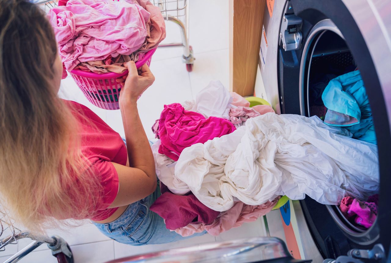Young beautiful woman washes and dries clothes in the laundry.