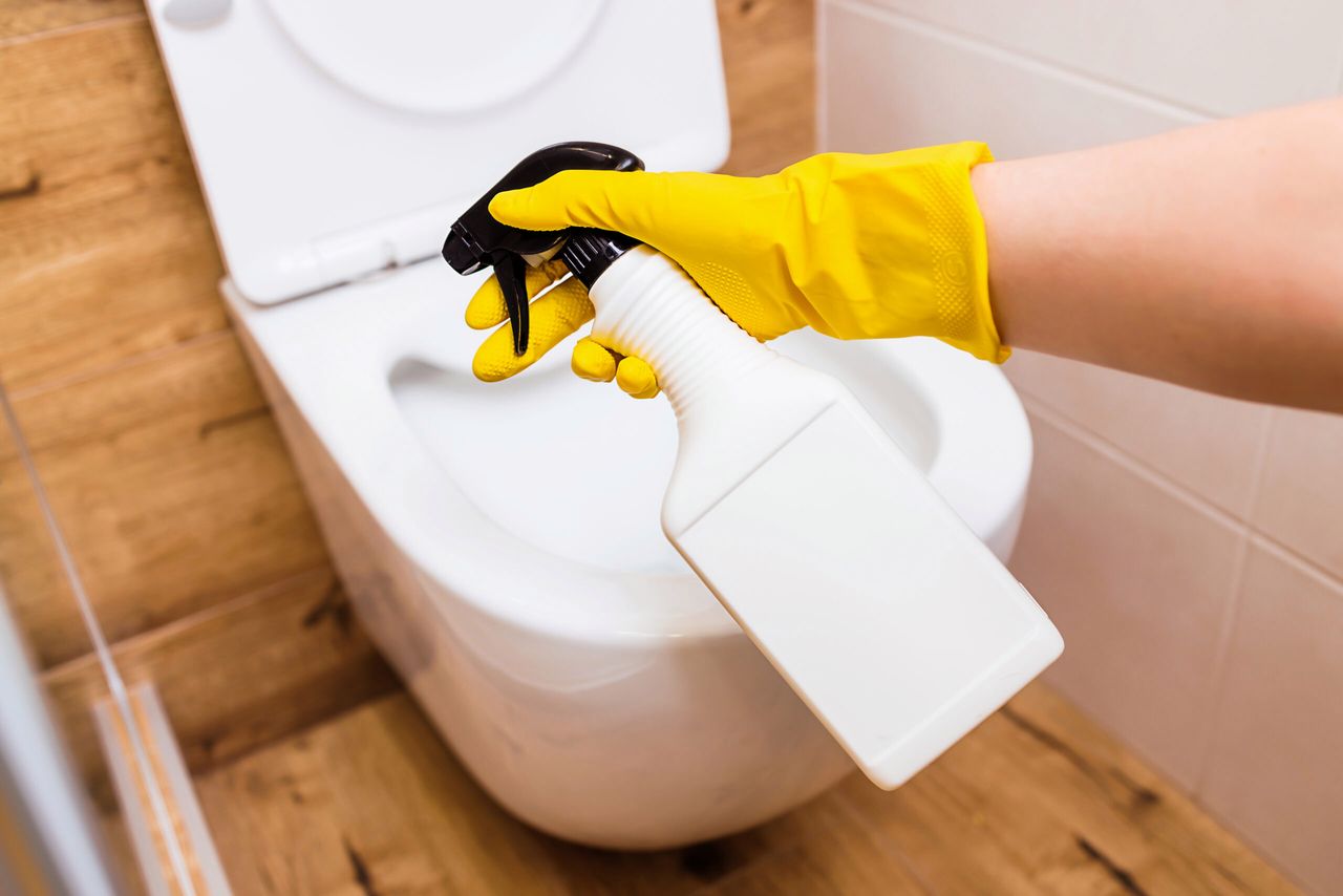 Mockup of a plastic white bottle with toilet cleaner, space for a logo. Close-up of female hands in protective gloves using cleaning solution and rags for cleaning, disinfection and toilet hygiene