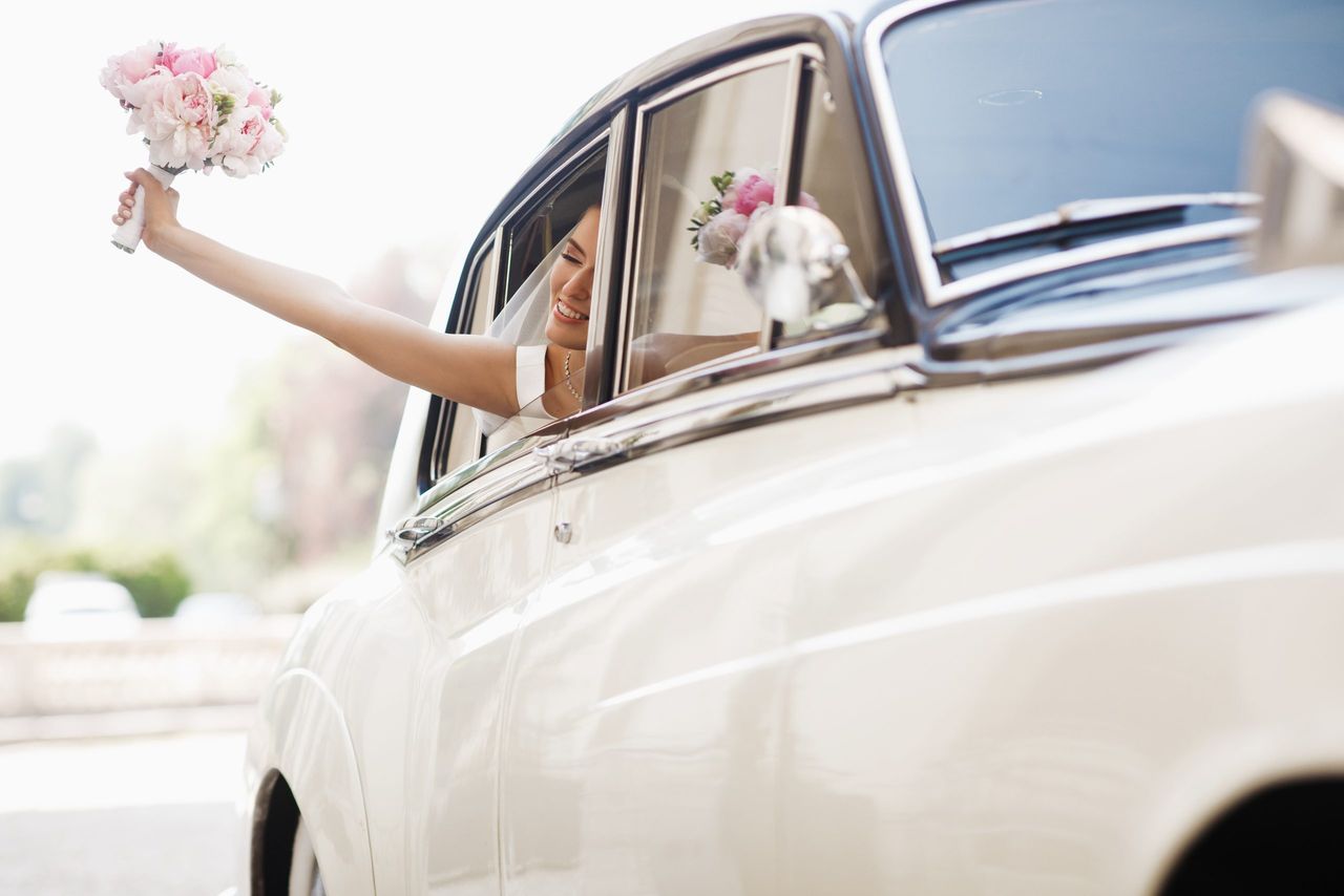 Beautiful bride sits with wedding bouquet in a retro car and has fun