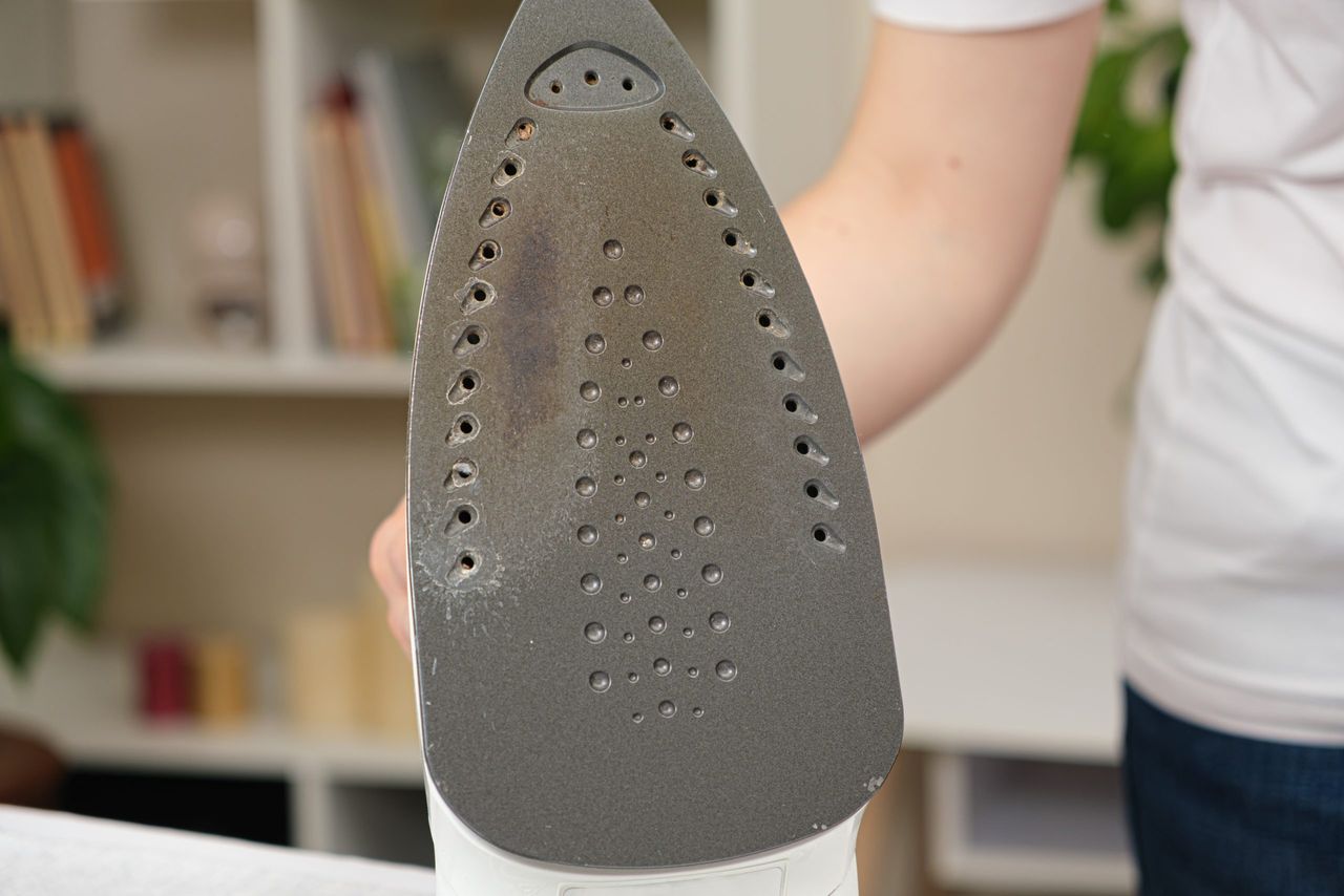 Damaged sole of the iron, brown stains and traces of burning with smoke and steam. Improper behavior during ironing clothes.