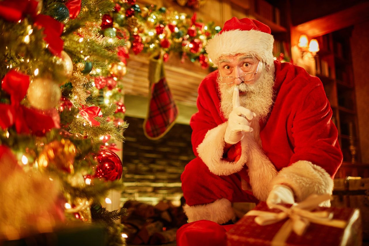 Portrait of traditional Santa Claus putting presents under Christmas tree in secret