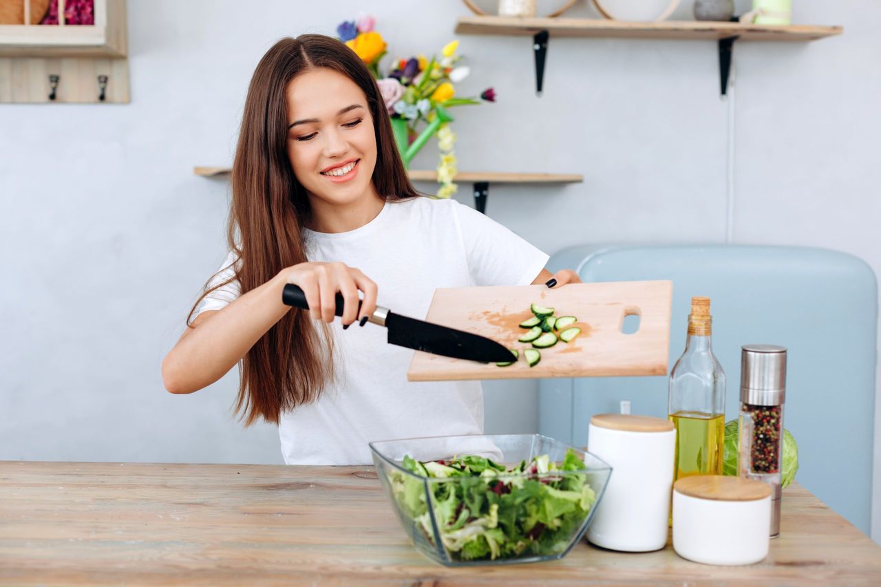 Beautiful, smiling, young woman slices cucumber into salad, healthy eating