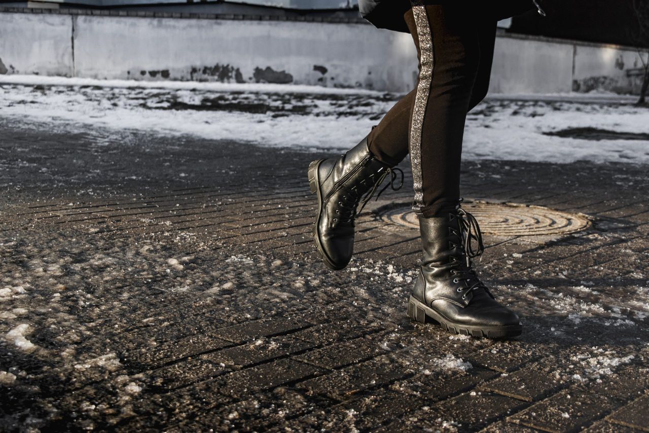 People walk on a slippery road made of melted ice. View of the legs of a man walking on an icy pavement. Winter road in the city. Injury after a fall on an icy road