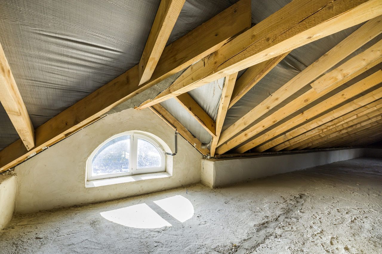 Attic of a building with wooden beams of a roof structure and a small window.