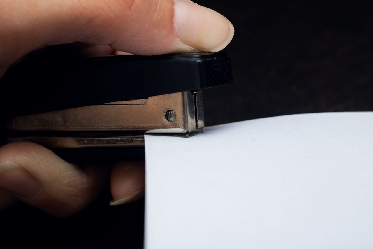 Black stapler and a sheet of paper in hand close up