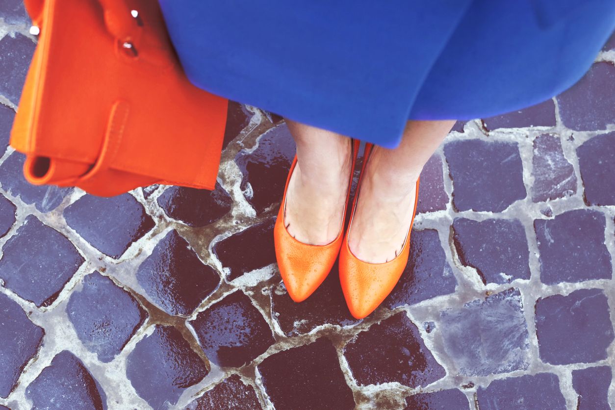 Women's legs in orange shoes. Bright orange shoes and bag. Blue coat, orange classic ladies shoes and tote bag. Rainy day. Street fashion. Street style. Business casual look. Autumn outfit. 