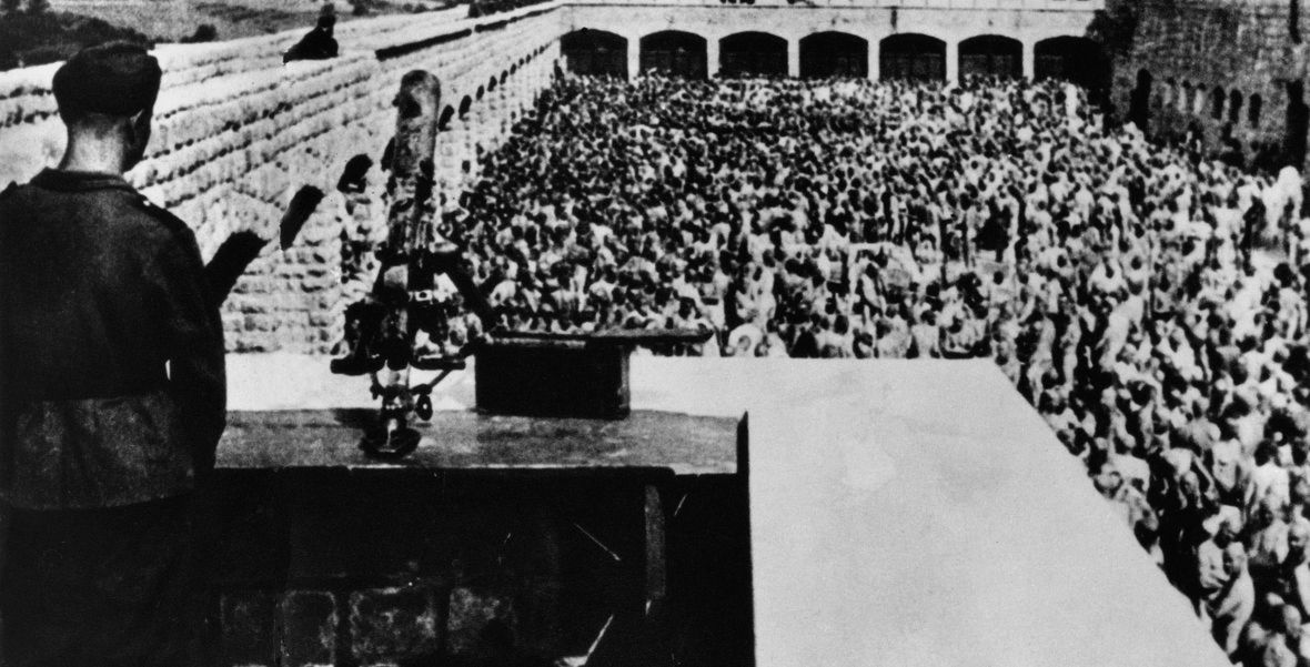 Strażnik obserwuje więźniów obozu koncentracyjnego Mauthausen-Gusen czekających nago na apel. Lata 40. XX wieku 