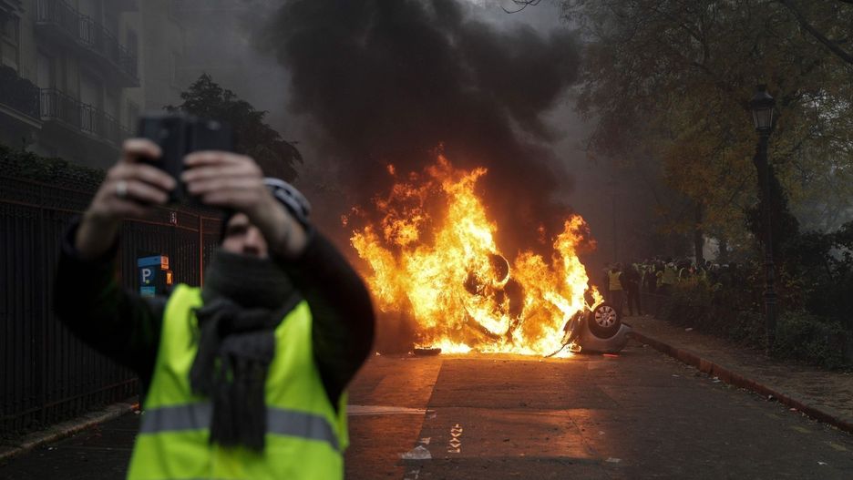Paryż.1 grudnia 2018 roku. Jeden z uczestników protestu "żółtych kamizelek" robi selfie na tle płonącego samochodu