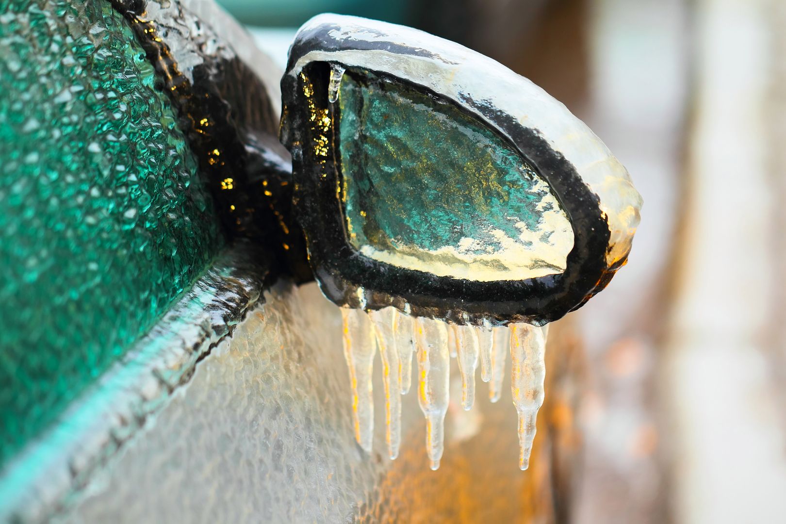 Car side mirror covered with ice and icicles, close up