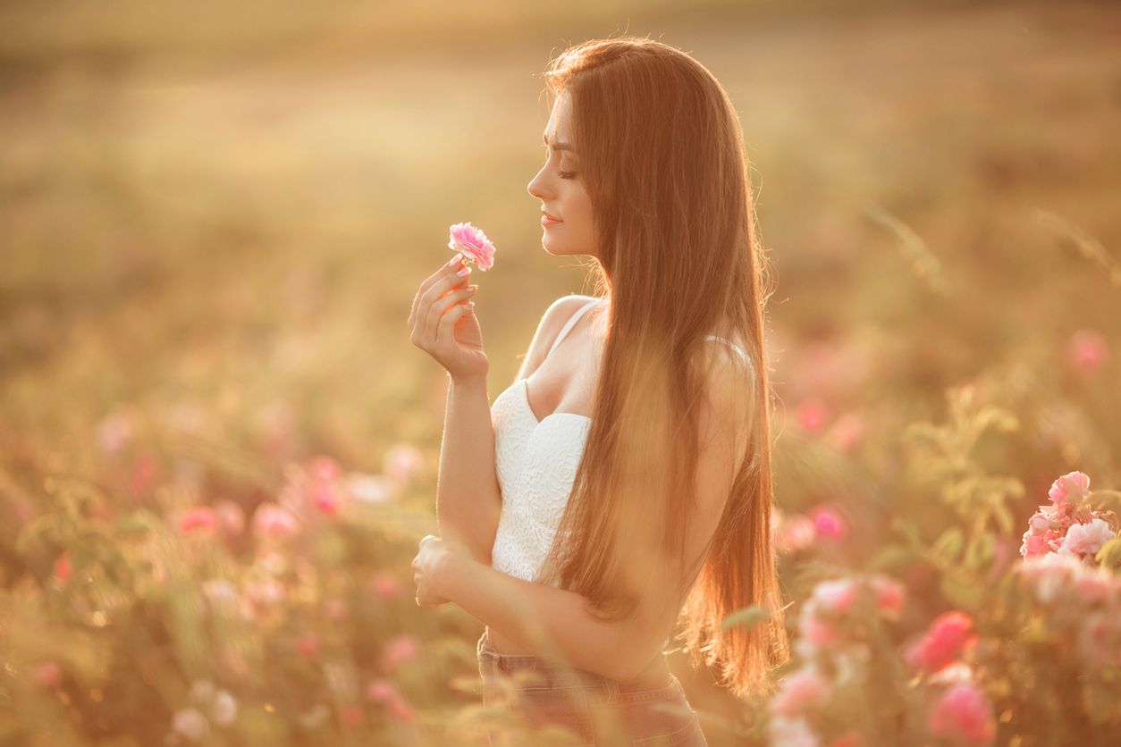 Beautiful young woman is wearing pink dress sitting in a blooming rose garden, summer time 