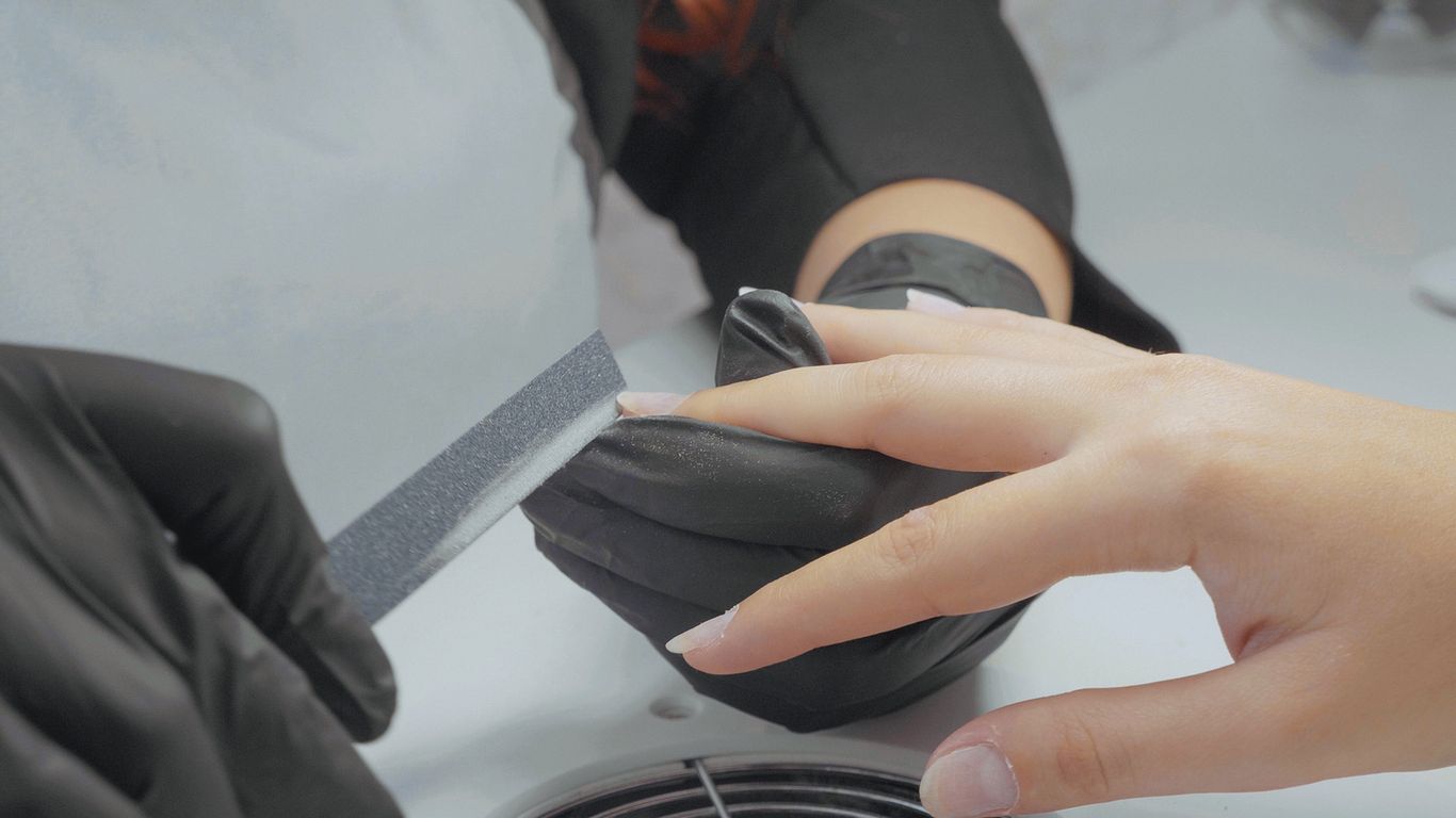 Close-up shot of manicurist filing nails of her female client. Beautician hand filing nails of young woman at beauty salon 