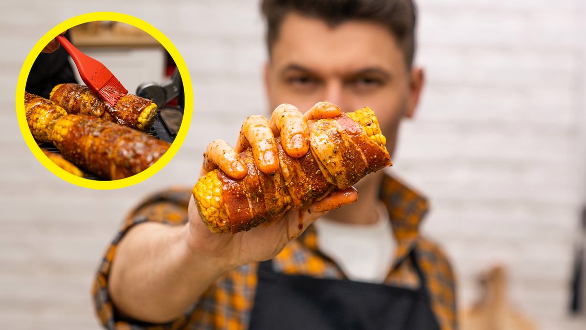 Mężczyzna trzyma w rękach grillowaną kolbę kukurydzy zawiniętą w boczek