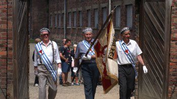 Byli więźniowie kierują się w stronę ściany śmierci na terenie dawnego obozu