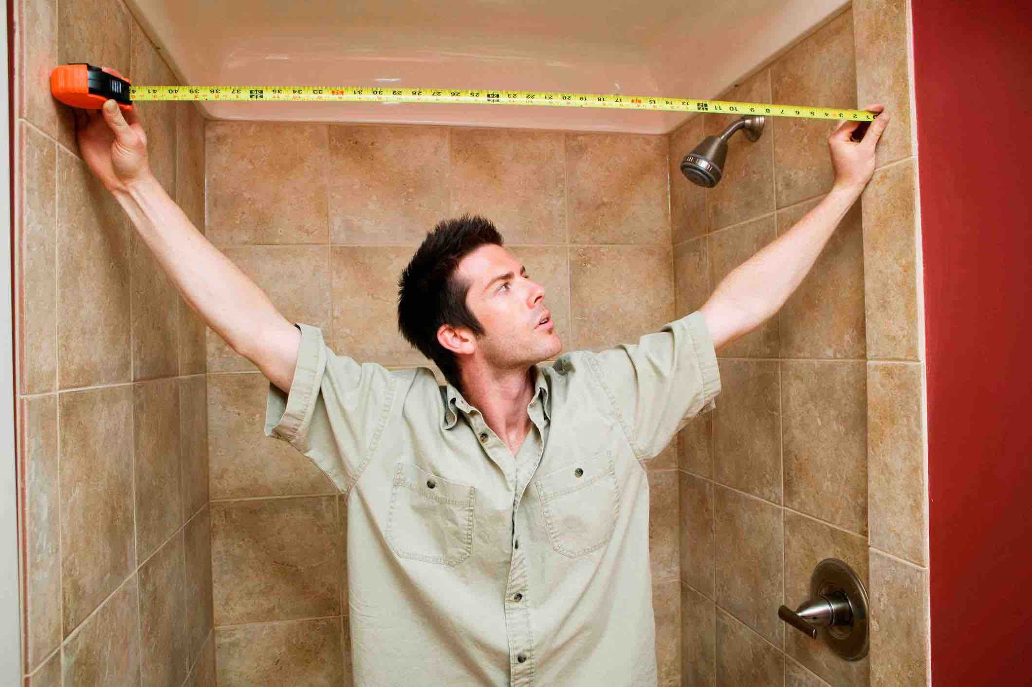 Young man measuring the width of the bathroom with a tape measure 